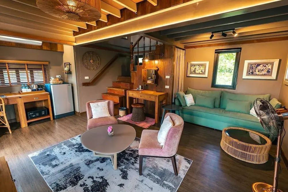 Gemütlicher Wohnbereich einer Villa mit grünem Sofa, Sesseln, Teppich und Holztreppe.