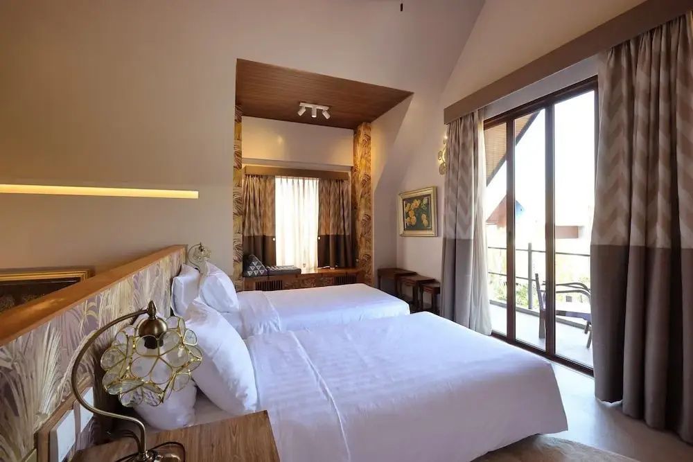 Helles Hotelzimmer mit zwei Einzelbetten, Dachschräge und großer Glastür zum Balkon.