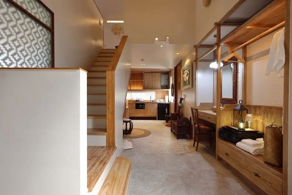 Zweistöckiger Wohnbereich mit Holztreppe, Schreibtisch und einer Küchenzeile im Hintergrund.