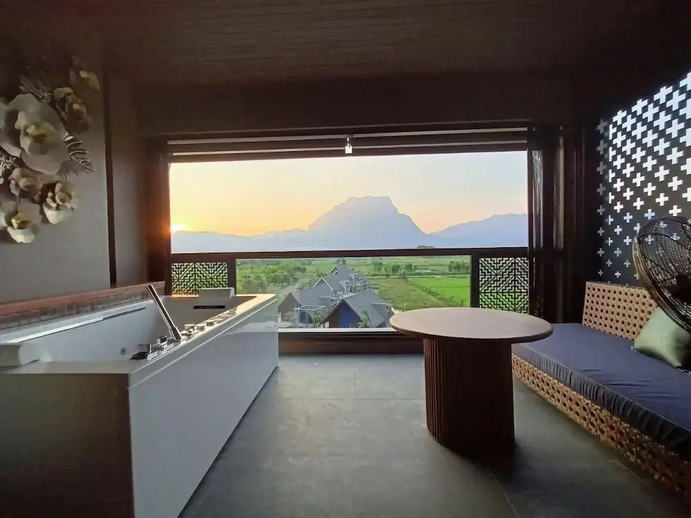 Überdachter Balkon mit Whirlpool, Holztisch und Weitblick auf Landschaft und Berge bei Sonnenuntergang.