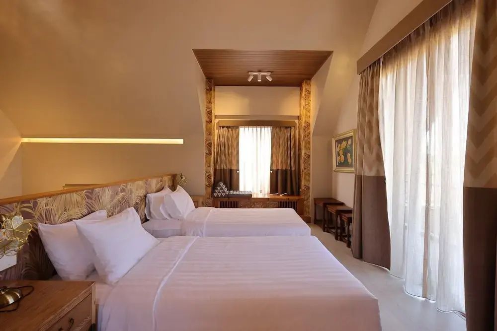 Helles Hotelzimmer mit zwei Einzelbetten und hoher Decke mit Holzelementen.