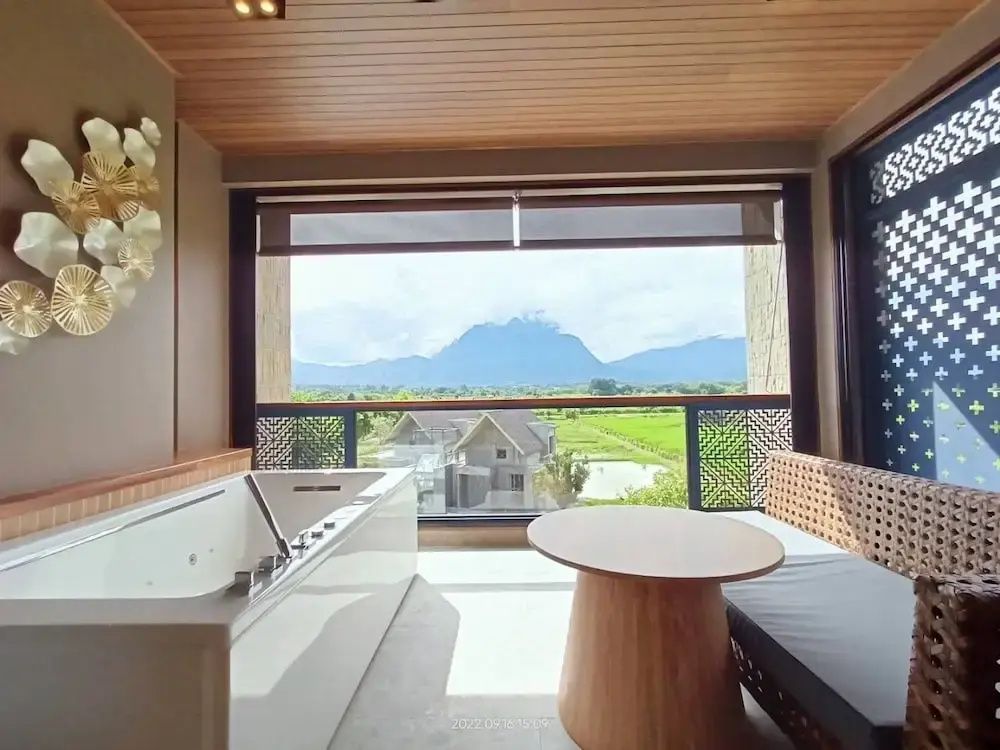 Überdachter Balkon mit Whirlpool, Sitzgelegenheit und Panoramablick auf grüne Felder und Berge.