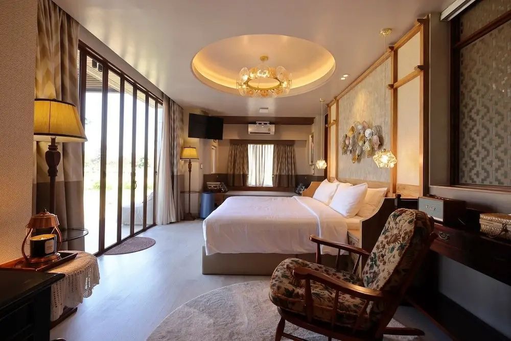 Großes Hotelzimmer mit Doppelbett, Sessel und rundem Deckenlicht.
