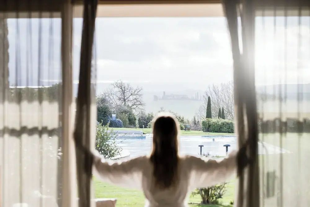 Person öffnet Vorhänge mit Blick auf die Landschaft und den Pool