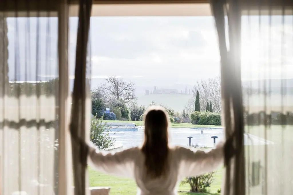 Frau im Bademantel betrachtet die Aussicht auf Garten und Pool