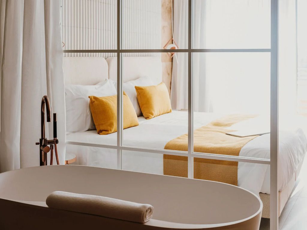 Elegantes Doppelzimmer mit warmen Farben und durchsichtiger Abtrennung zum Badezimmer