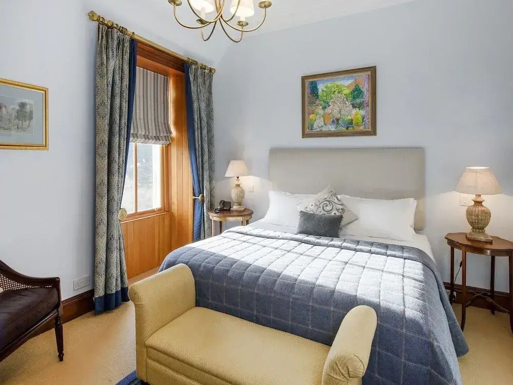 Helles Schlafzimmer mit Doppelbett, gepolsterter Bank und Vorhängen vor einem Fenster