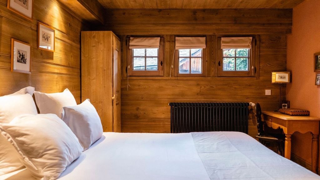 Schlichtes Schlafzimmer mit Holzwänden und drei Fenstern