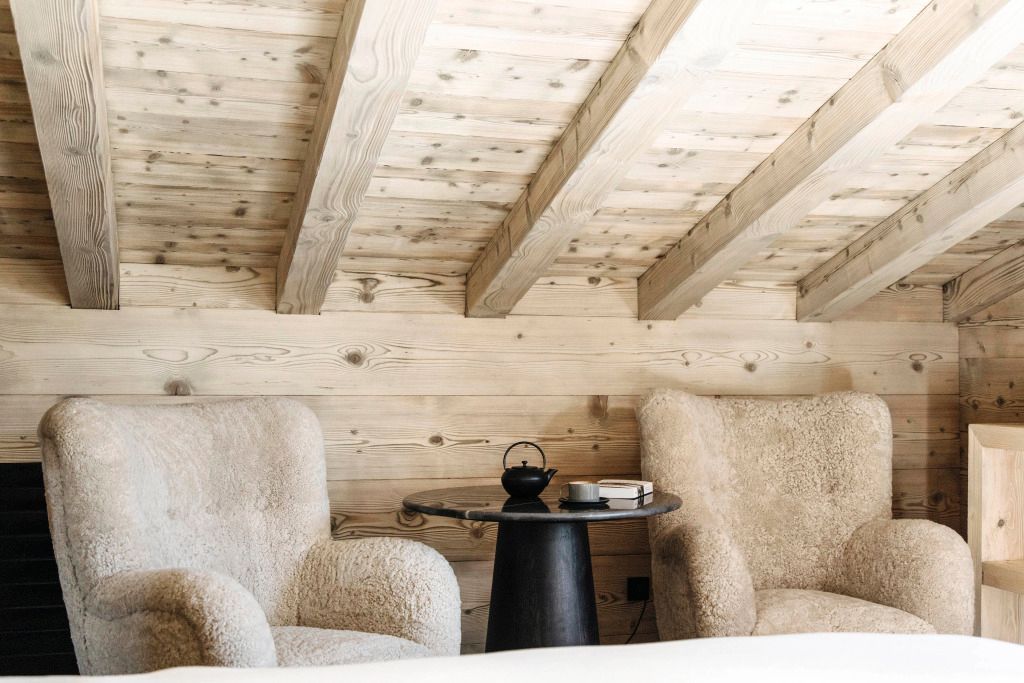 Gemütliche Sitzecke mit zwei Sesseln und kleinem Tisch unter Holzbalkendecke im Schlafzimmer.