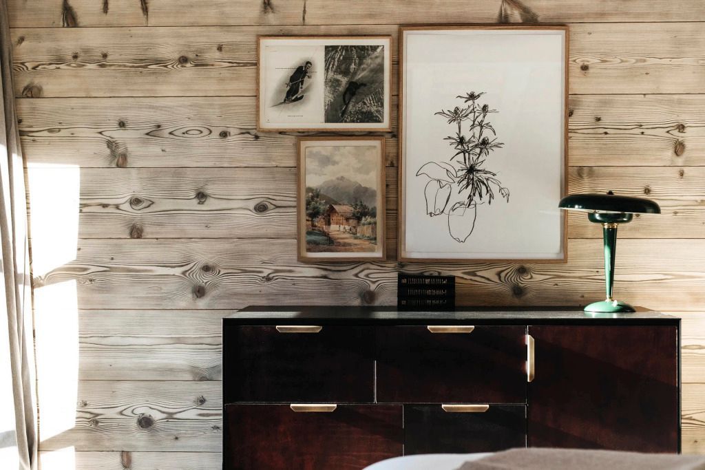 Dekorative Kunstwerke hängen an einer Holzwand über einer stilvollen Kommode.