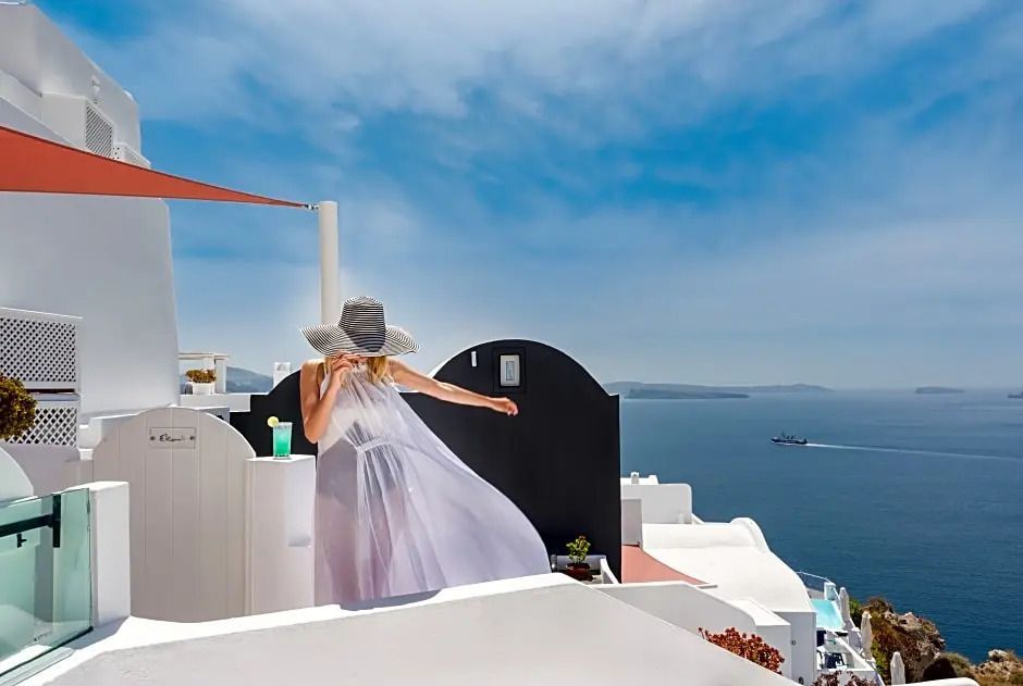 Frau in weißem Kleid auf Terrasse mit atemberaubendem Meerblick und klarem Himmel.