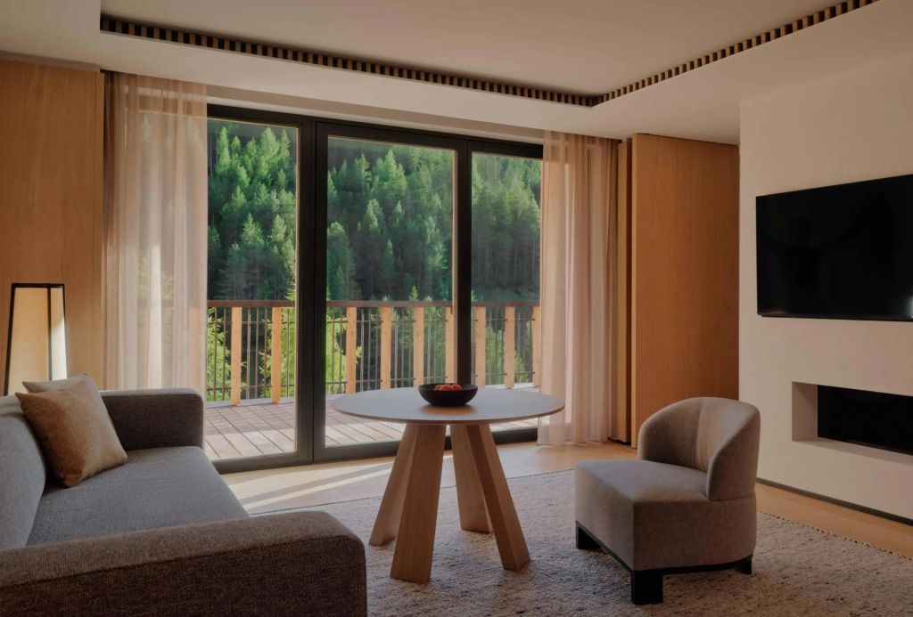 Helles Wohnzimmer einer Suite mit großen Fenstern und Waldblick