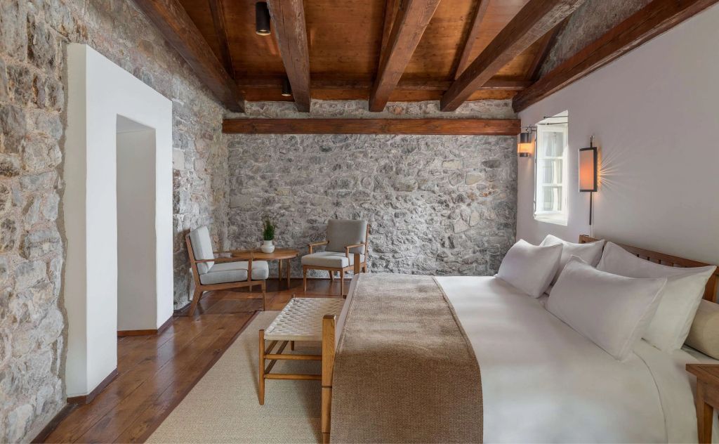 Schlafzimmer mit Holzbalken, großen Fenstern und luxuriösem Doppelbett