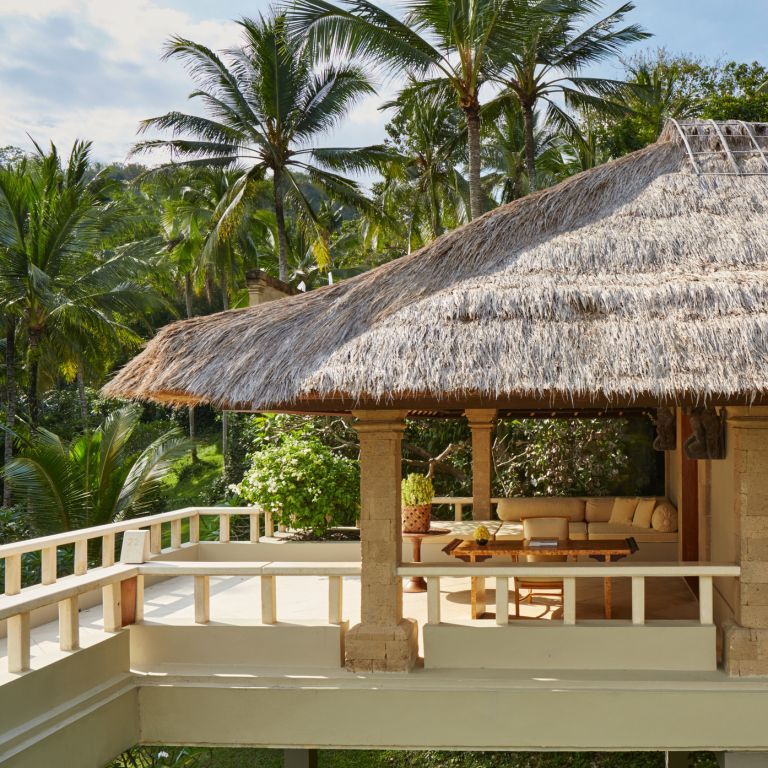 Balinesische Terrasse mit Strohdach und Sitzbereich umgeben von Palmen im Amankila Hotel