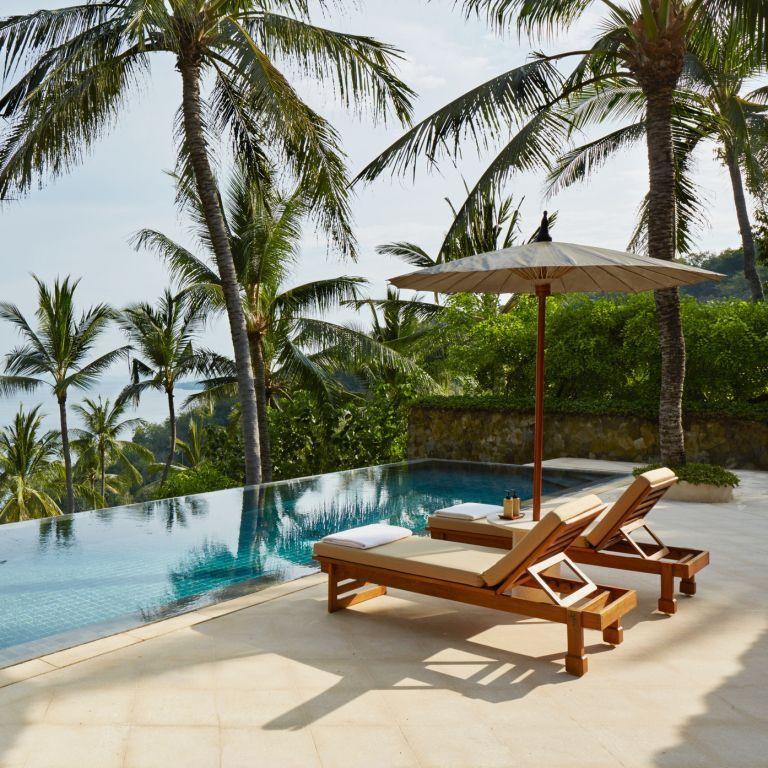 Infinity Pool mit Meerblick und Sonnenliegen unter Palmen.
