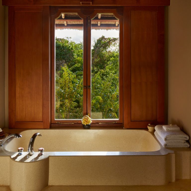 Luxuriöse Badewanne mit Blick auf den grünen Garten durch ein großes Fenster.