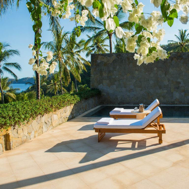 Private Terrasse mit Liegen und Meerblick umgeben von Blüten und Palmen