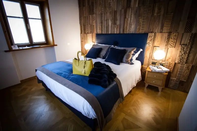 Elegantes Doppelbett mit blauen Kissen und Holzakzentwand im klassischen Hotelzimmer