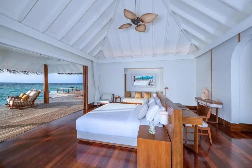 Schlafzimmer mit weißen Bettlaken und Blick auf eine Terrasse über dem Wasser.