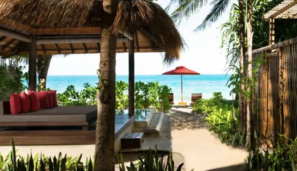 Strandblick von der Terrasse mit Sonnenliegen und rotem Sonnenschirm