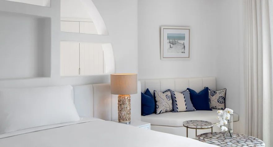 Gemütlicher Sitzbereich im Fira Doppelzimmer mit dekorativen Kissen und Kunst im Anantara Santorini.