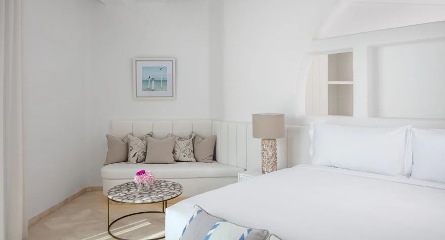 Gemütliche Sitzecke mit Kunstwerk und Bett in der Oia Suite.