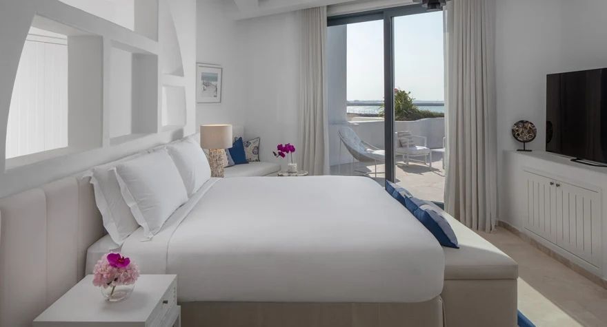 Modernes Doppelzimmer mit Meerblick und Balkon, eleganter weißer Einrichtung.