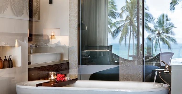 Luxuriöse Badewanne mit Blick auf den Ozean und umliegende Palmen