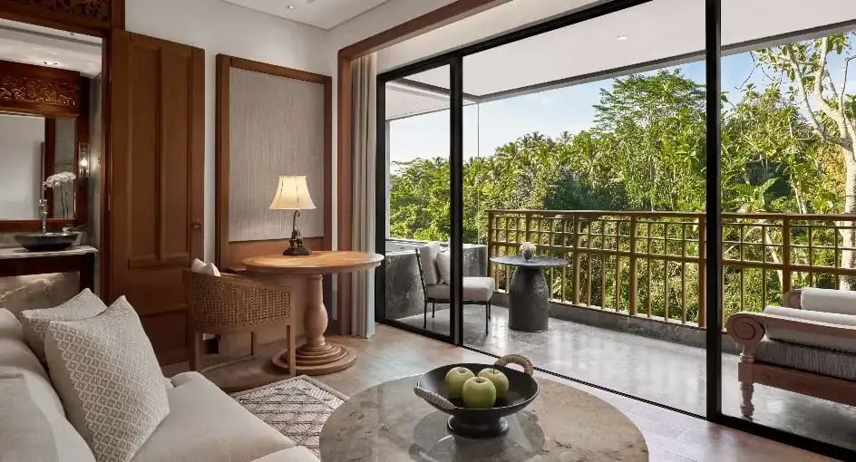 Gemütlicher Sitzbereich im Zimmer mit Balkon und Waldsicht im Hintergrund.