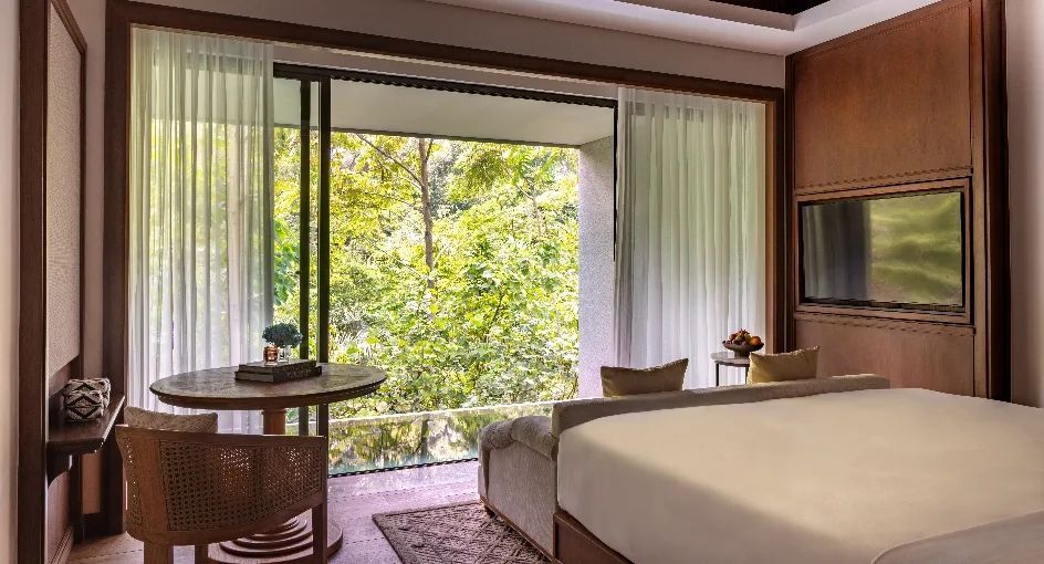 Helles Schlafzimmer mit Blick auf einen dichten Wald durch große Fenster.