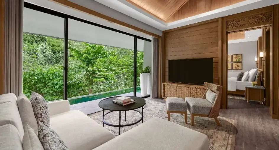 Gemütliches Wohnzimmer mit Blick auf üppiges Grün und Pool.