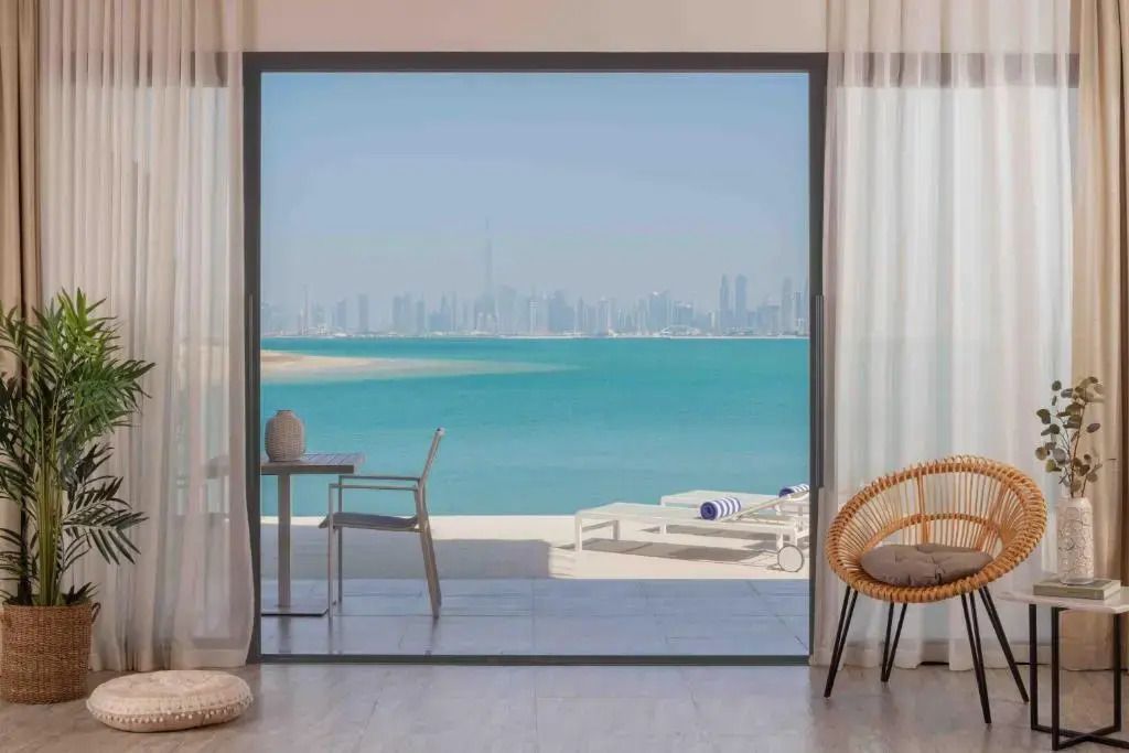 Blick von der Suite auf die Terrasse mit Sonnenliegen und das Meer im Hintergrund.