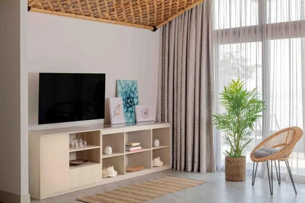 Wohnbereich mit großem Fernseher und Regal. Zugang zu einem lichtdurchfluteten Raum.