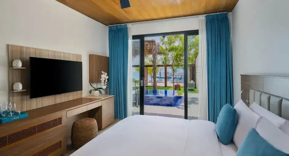 Zimmer mit Doppelbett, Blick auf den privaten Pool und Garten durch große Fenster.