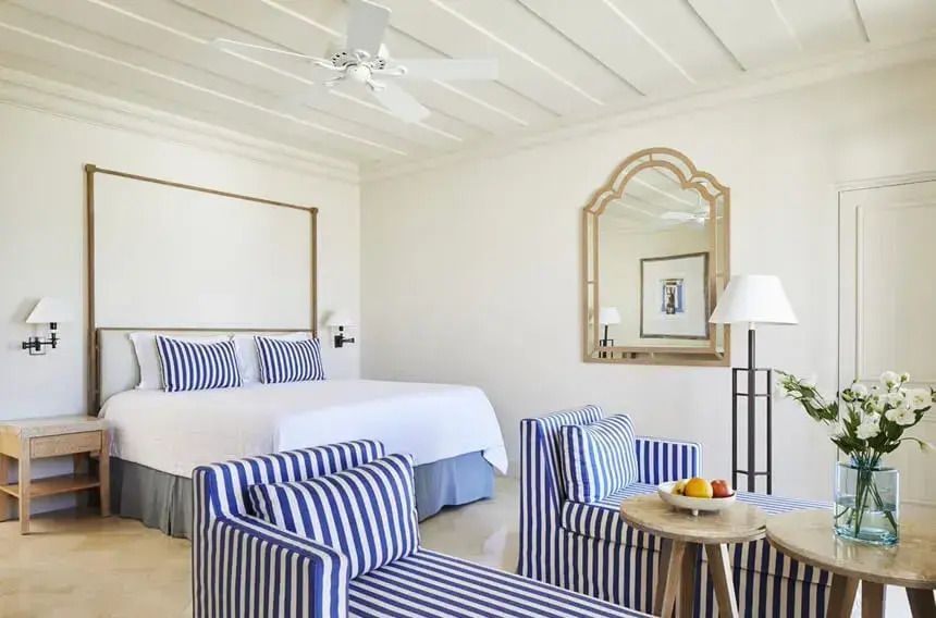 Elegantes Doppelbett in einer Suite mit gestreiften Stühlen und großem Spiegel