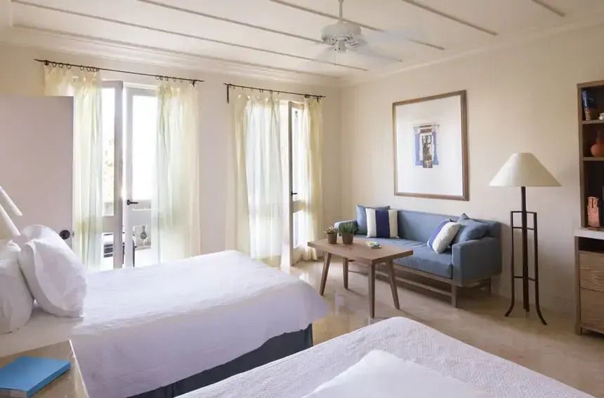 Geräumige Suite mit zwei Betten, Sofa und Zugang zum Balkon mit frischen Gardinen.