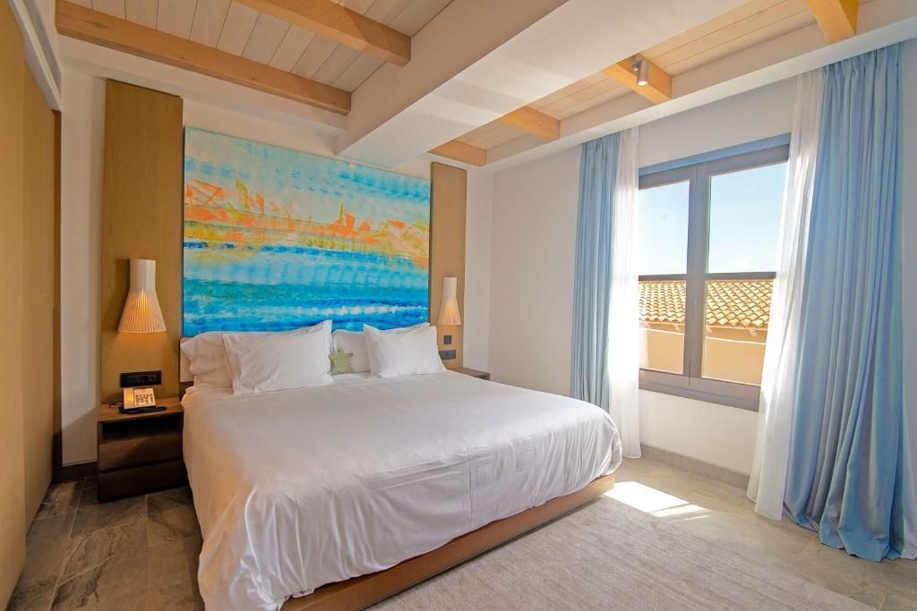 Helles Schlafzimmer mit großem Doppelbett und Kunstwerk über dem Bett. Meerblick durch Fenster.