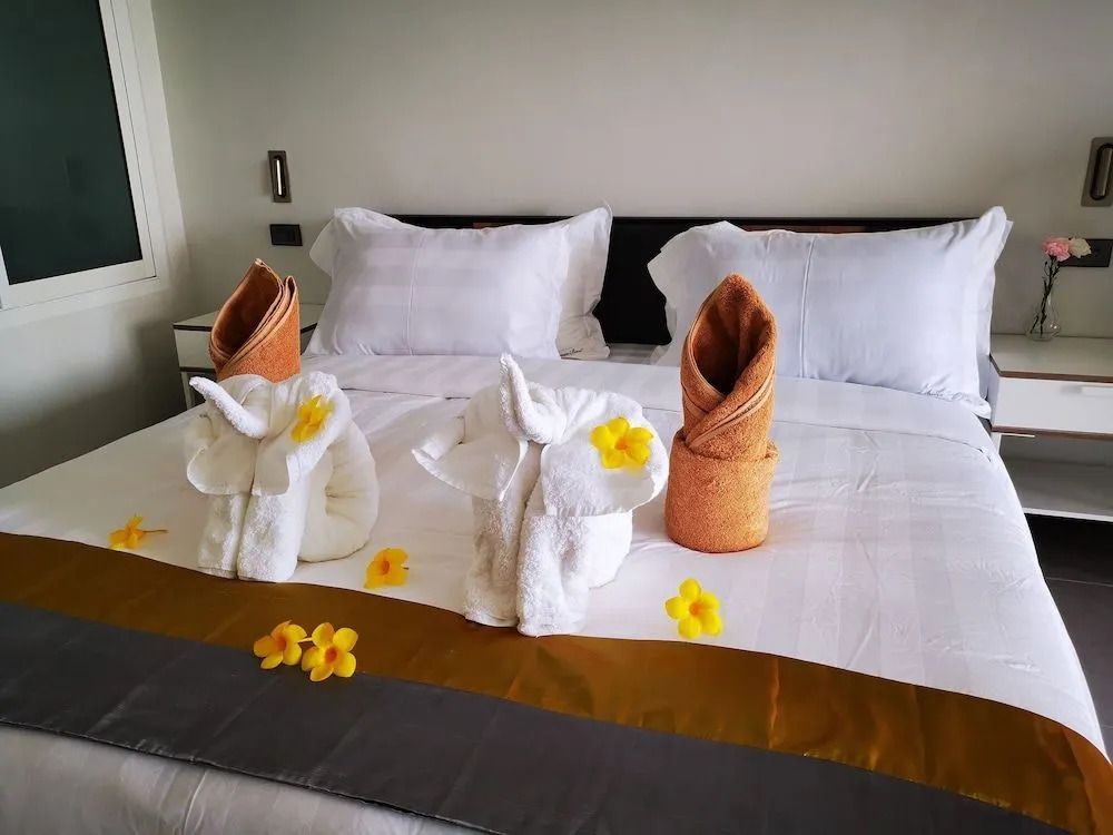 Detailaufnahme eines Hotelbettes mit kunstvoll gefalteten Handtüchern und Blütendekoration