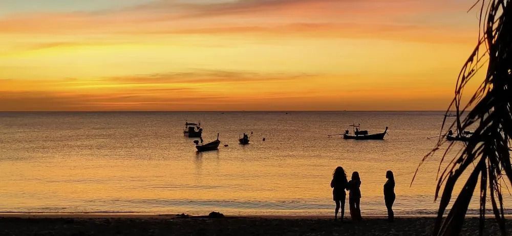 Sonnenuntergang am Strand mit Booten und silhouettierten Personen