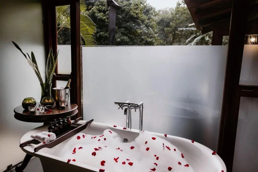 Luxuriöse Badewanne mit Rosenblättern, Blick in tropische Natur