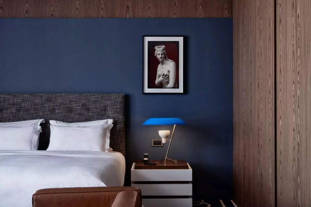 Detailansicht des Nachttisches mit blauer Lampe und klassischem Kunstwerk über dem Bett