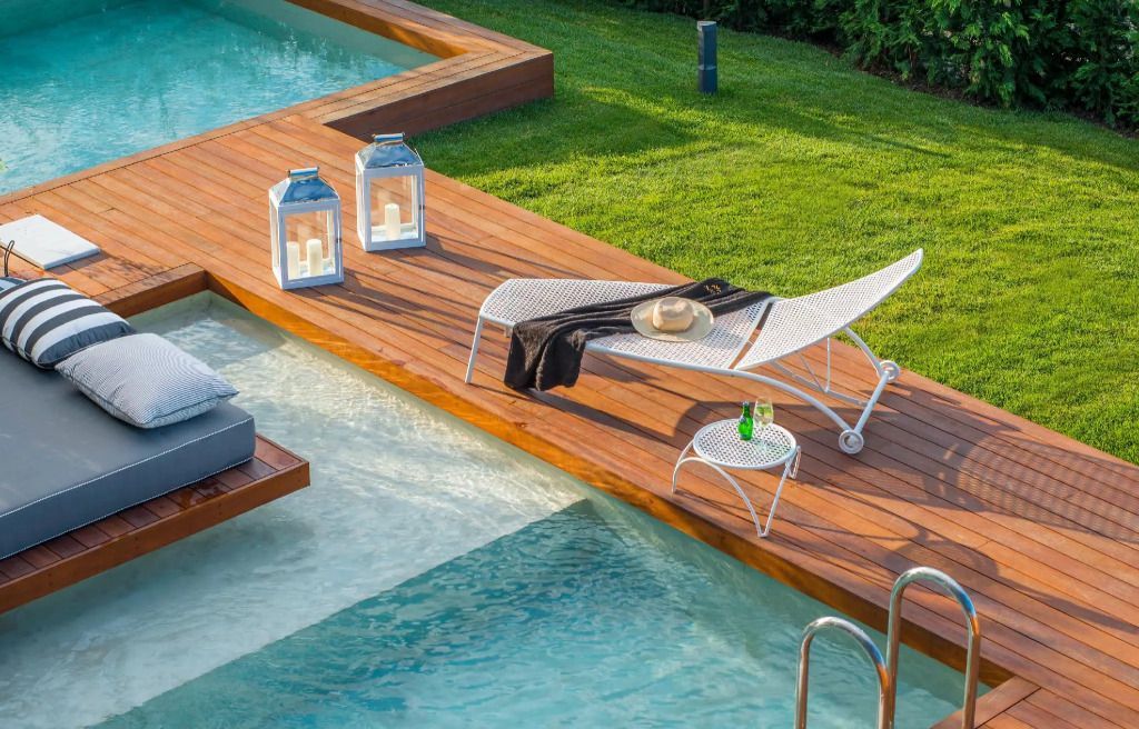 Sonnenliegen neben einem luxuriösen Pool mit Holzdielen und Gartenblick
