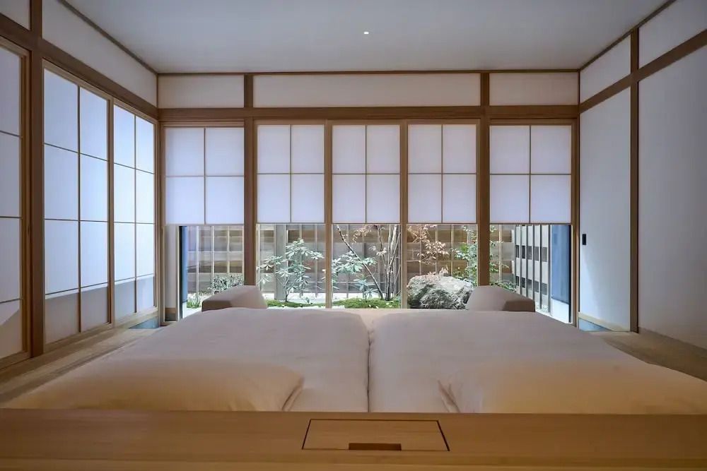 Doppelbett mit Blick auf einen begrünten Innenhof durch bodentiefe Fenster