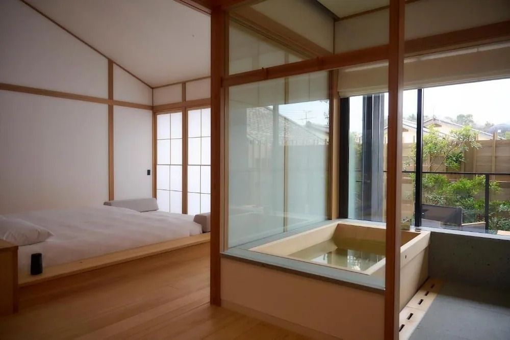 Blick auf Badewanne aus Glaswand mit Zugang zum minimalistisch eingerichteten Schlafbereich