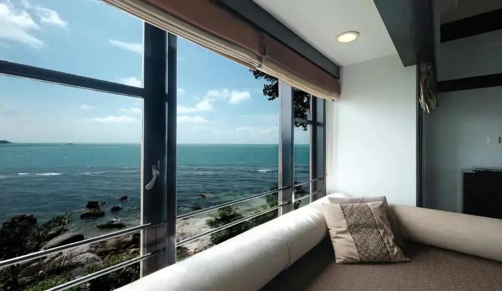 Ausblick von einem Fenster auf das Meer mit blauem Himmel und einigen Wolken