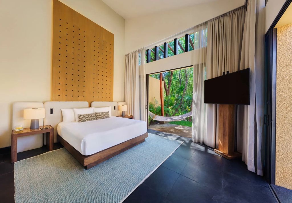 Elegantes Schlafzimmer mit großem Fenster und Blick auf tropische Vegetation