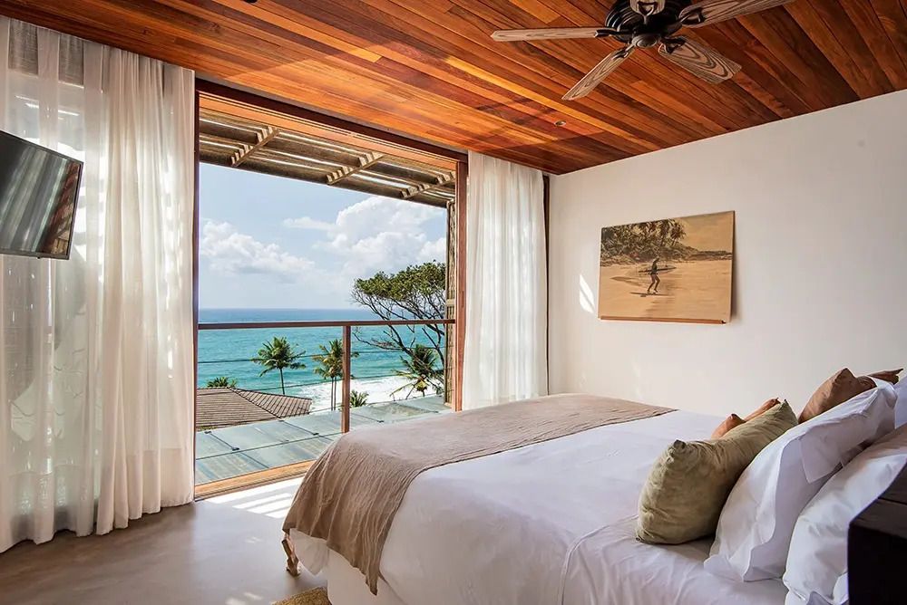 Zimmer mit Doppelbett, Holzbalkendecke und Meerblick durch ein großes Fenster