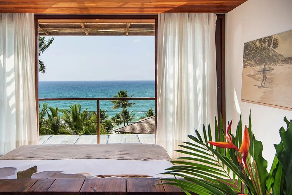 Schlafzimmer mit Bett und großem Fenster mit Blick auf Palmen und das Meer