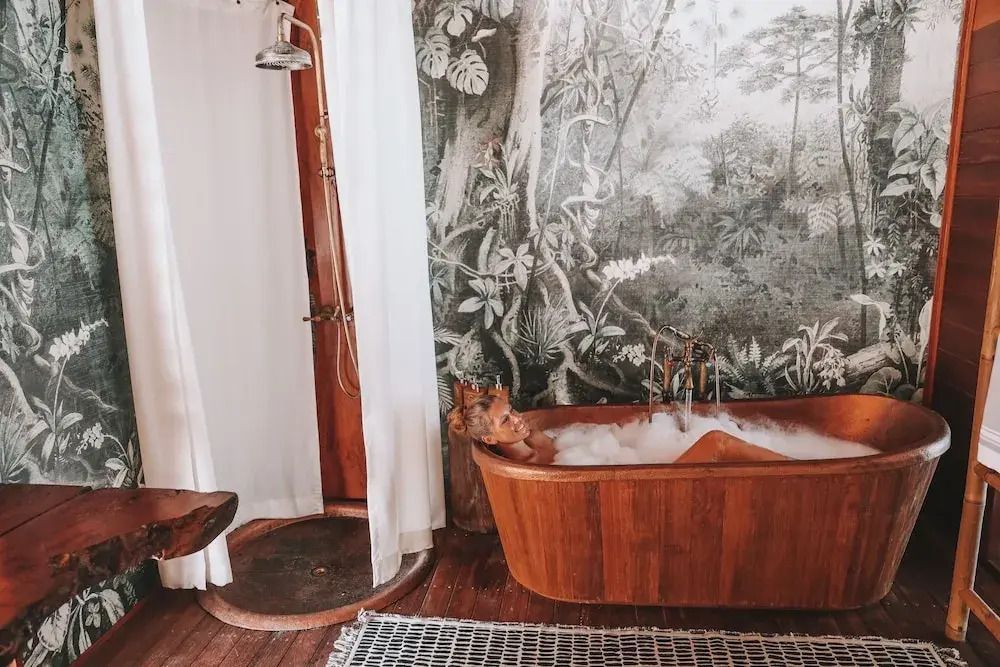 Holzbadewanne umgeben von Naturmotiven und offener Dusche im Bawah Reserve