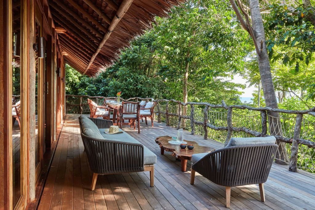 Großer Balkon mit stilvollen Holzsofas und üppigem Grün im Hintergrund.